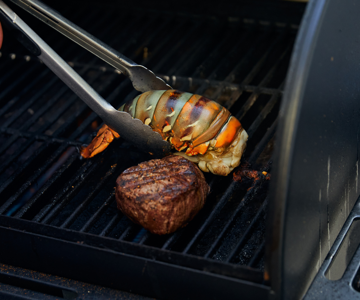 Grilling lobster and steak on a barbecue with tongs.