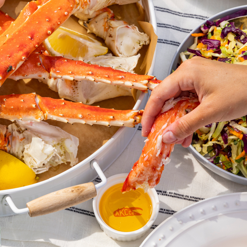 Person dipping a crab leg into a yellow sauce with a side of salad on a white tablecloth.