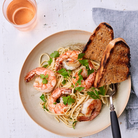 Plate of pasta with shrimp and toast on a white surface