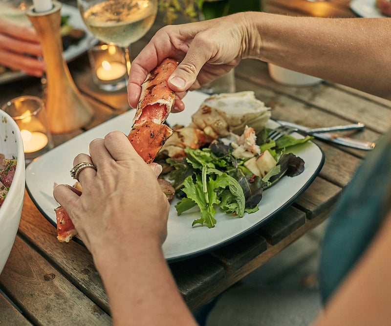 Woman's hands cracking crab legs over her plate at the dinner table.