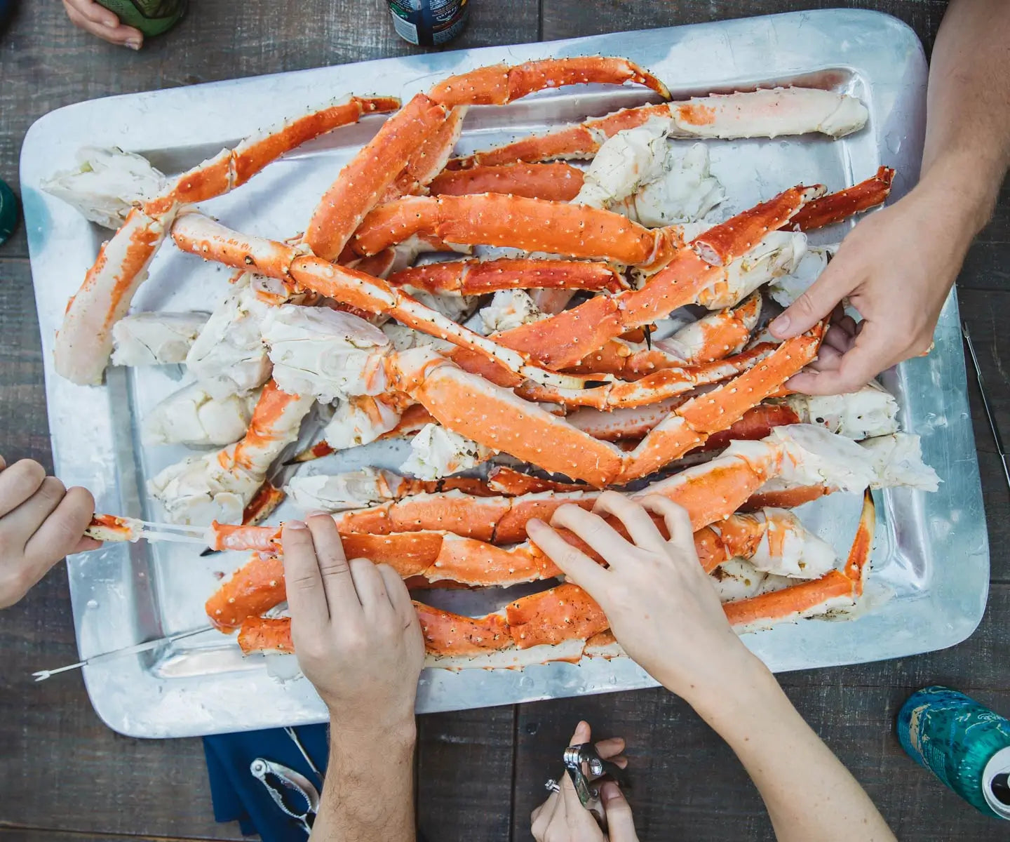 hands grabbing bright orange king crab legs off of a silver platter