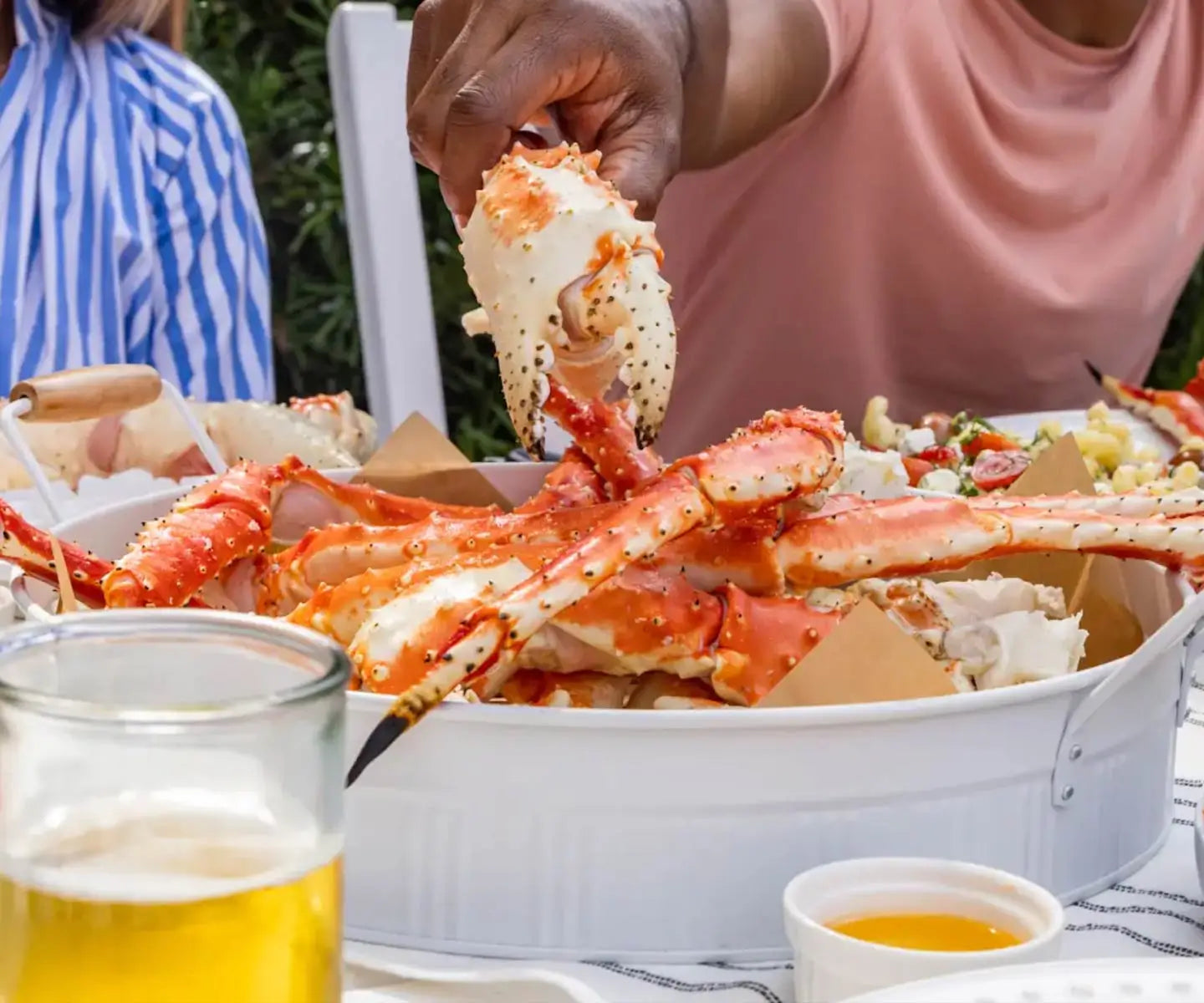crab claw being grabbed from a large platter surrounded by butter
