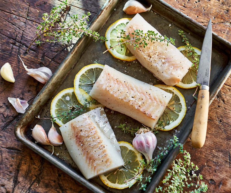 Fish on baking sheet with lemons and seasoning ready to go in the oven.