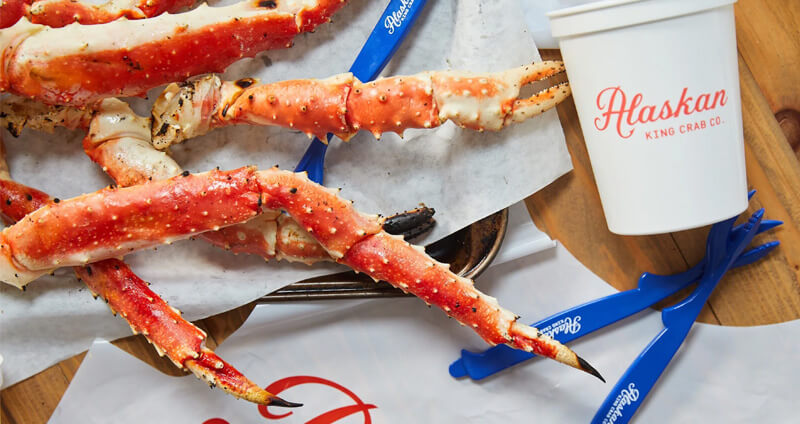 Table setting with Alaskan King Crab Co. paper copy, crackers and bib by a plate with crab lets.