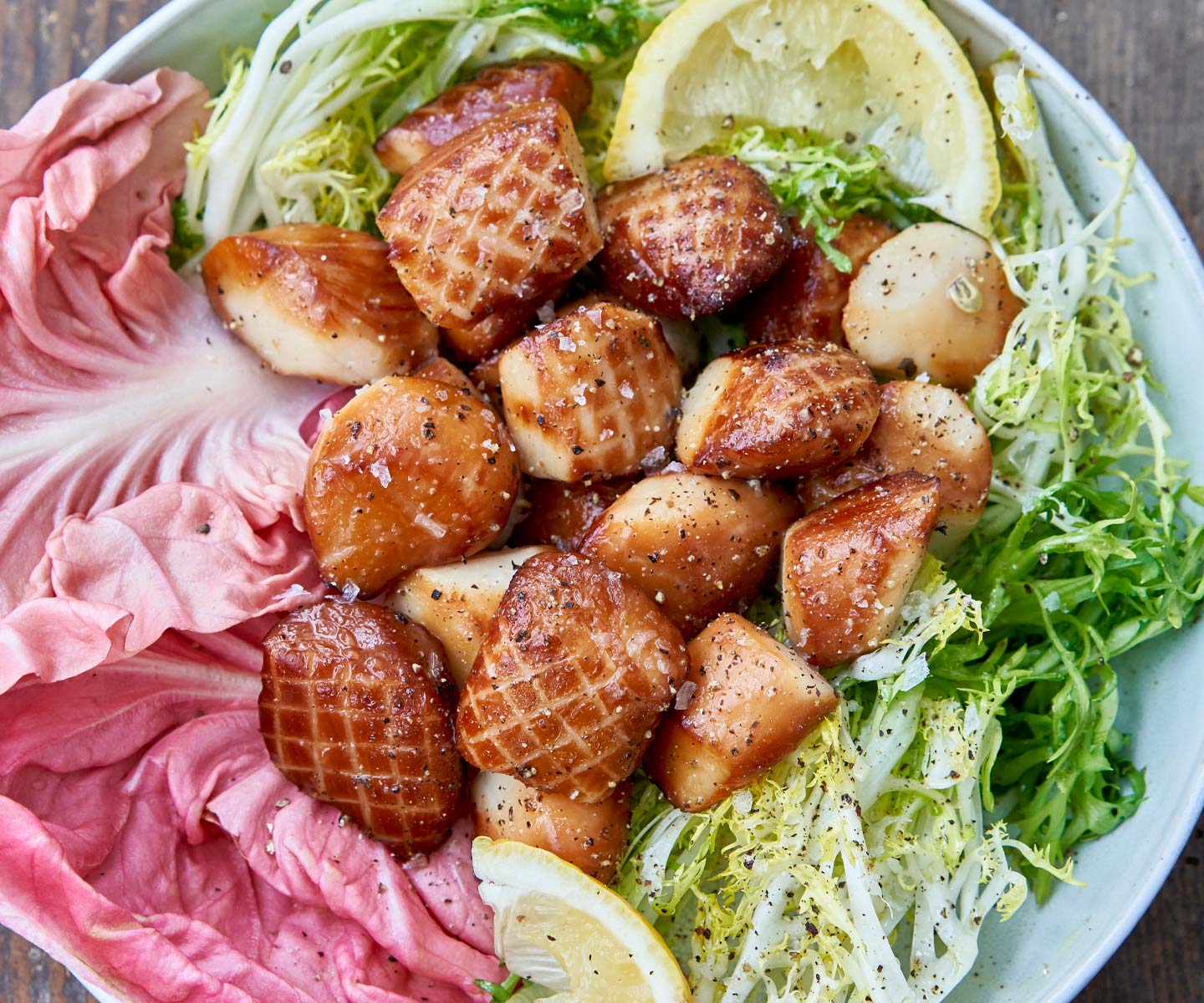 Seafood dish with scallops, pink fish cake, and lemon wedges on a bed of greens.