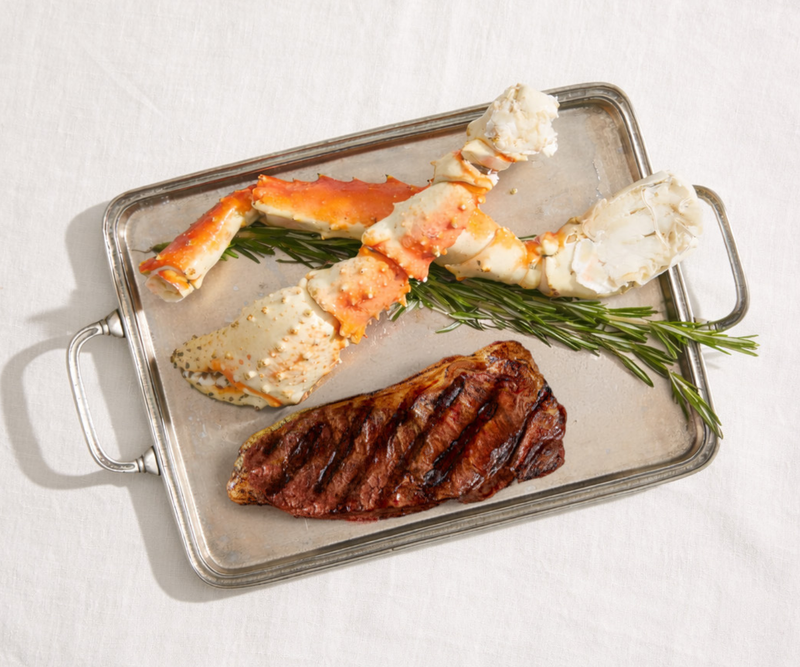Grilled steak with crab legs on a metal tray on a white background