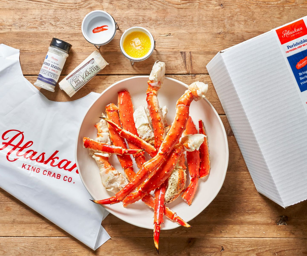Alaskan King Crab Co. crab legs on a plate with seasonings and a box on a wooden surface.