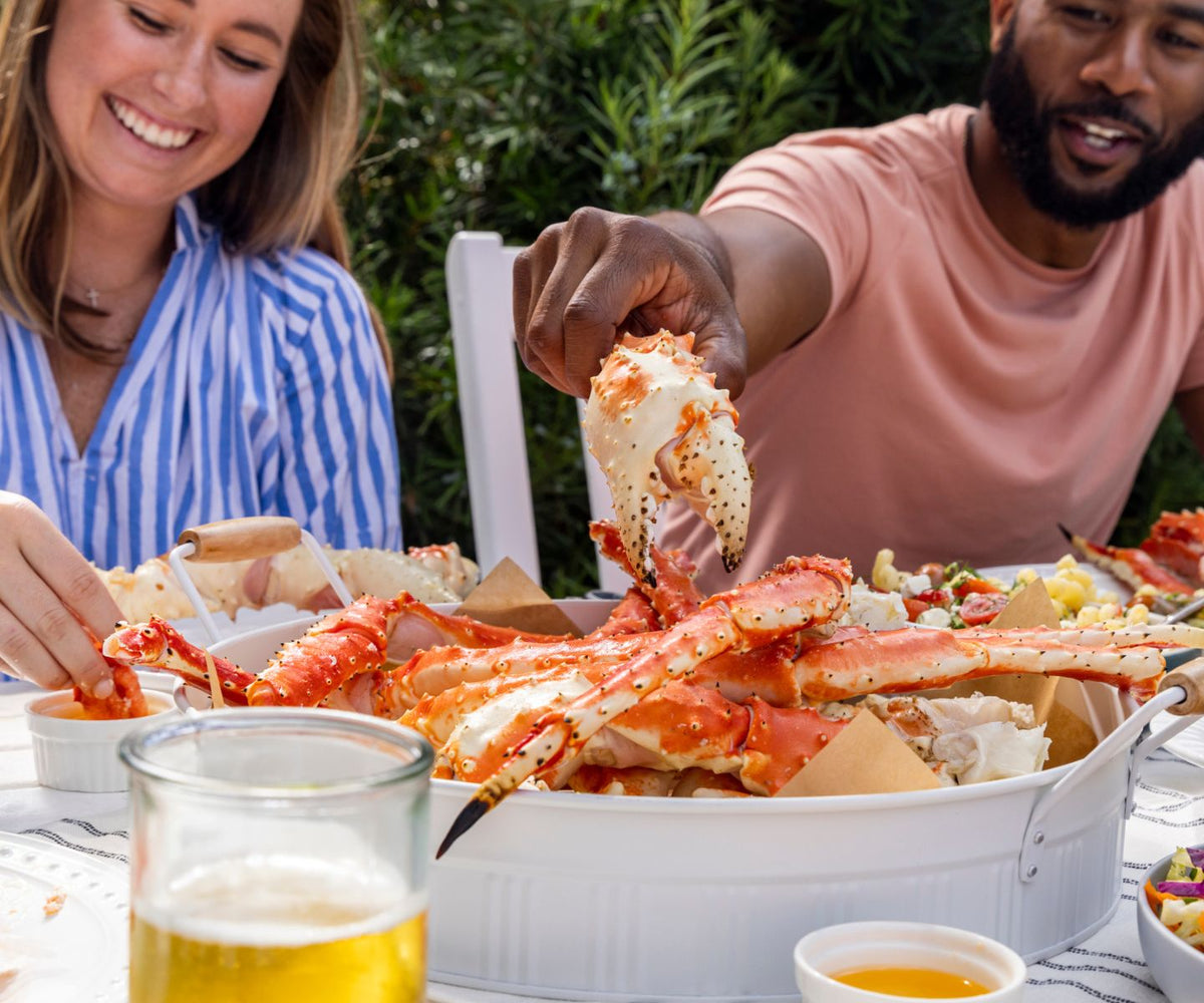 Two people enjoying a seafood meal outdoors, with a focus on a large platter of crab legs.