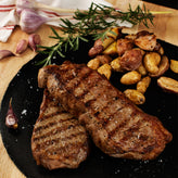 Grilled steak with roasted potatoes on a black slate plate, garnished with rosemary.