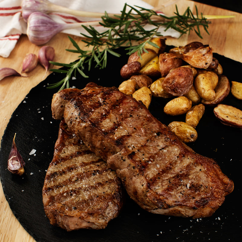 Grilled steak with roasted potatoes on a black slate plate, garnished with rosemary.