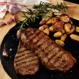 Grilled steak with roasted potatoes on a black slate plate, garnished with rosemary.