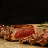 Sliced steak on a wooden cutting board with a dark background