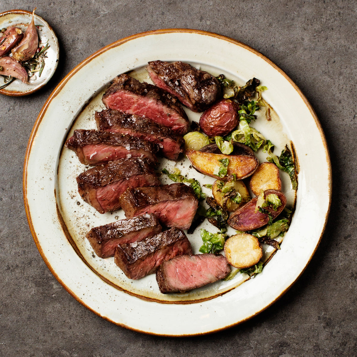 Plated dish of sliced steak with roasted vegetables on a textured surface