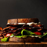 Deluxe sandwich with bacon, lettuce, and tomato on a wooden board against a dark background