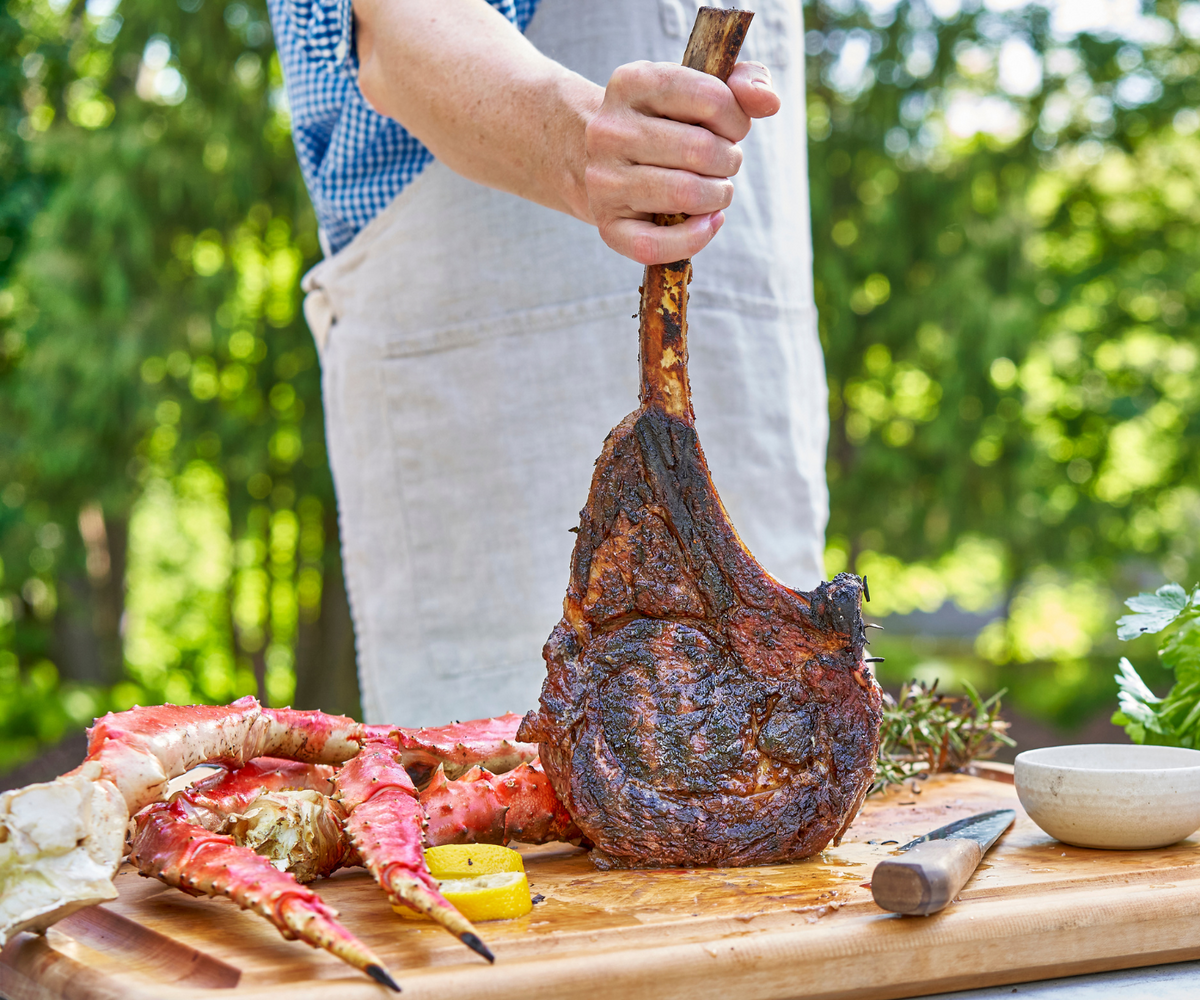 Chef holding a large Tomahawk Ribeye up with King Crab legs on the cutting board.