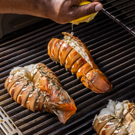 Lobster tails being grilled with a hand squeezing lemon over them.