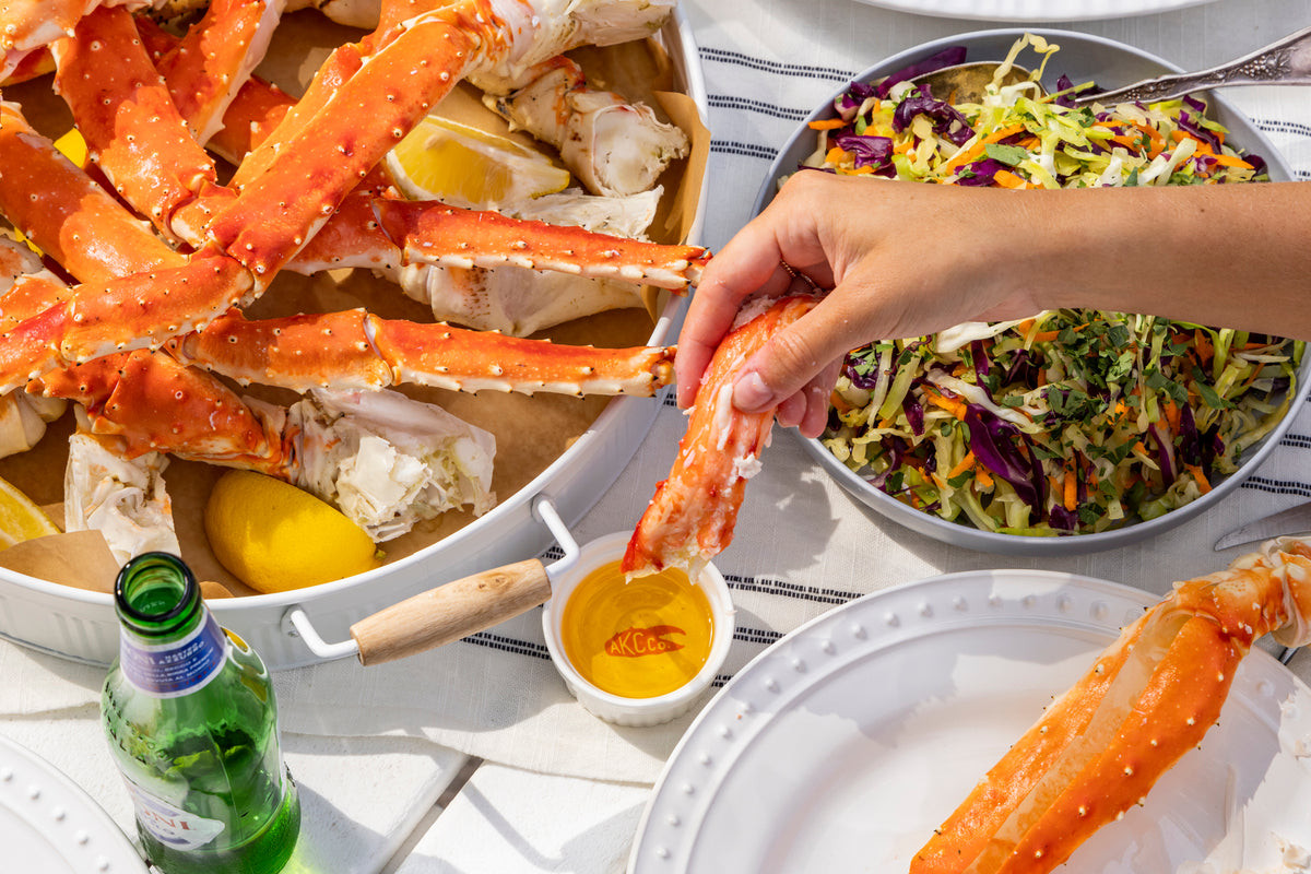 Person holding a crab leg with a dining table full of food including salad and drinks.