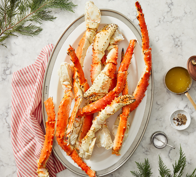 Platter of crab legs on a marble surface with herbs and a towel.