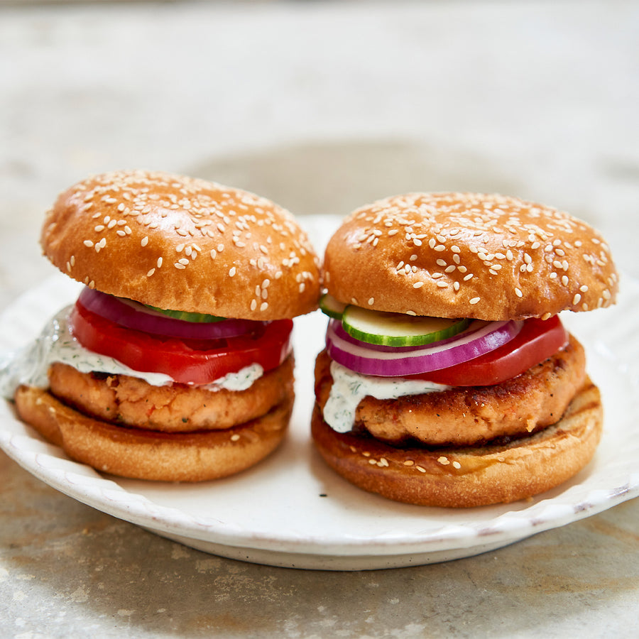 Two salmon burgers with buns, lettuce, tomato, and onion on a white plate.