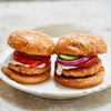 Two salmon burgers with buns, lettuce, tomato, and onion on a white plate.