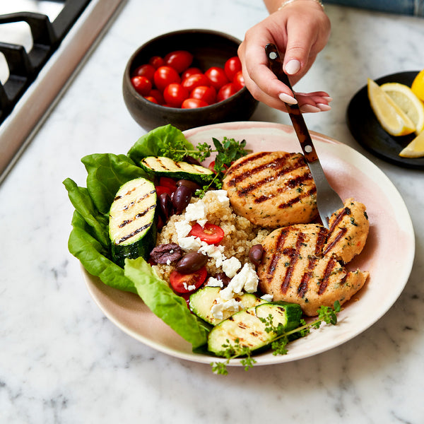Plated salad with grilled salmon patties, zucchini, and cherry tomatoes on a marble surface.