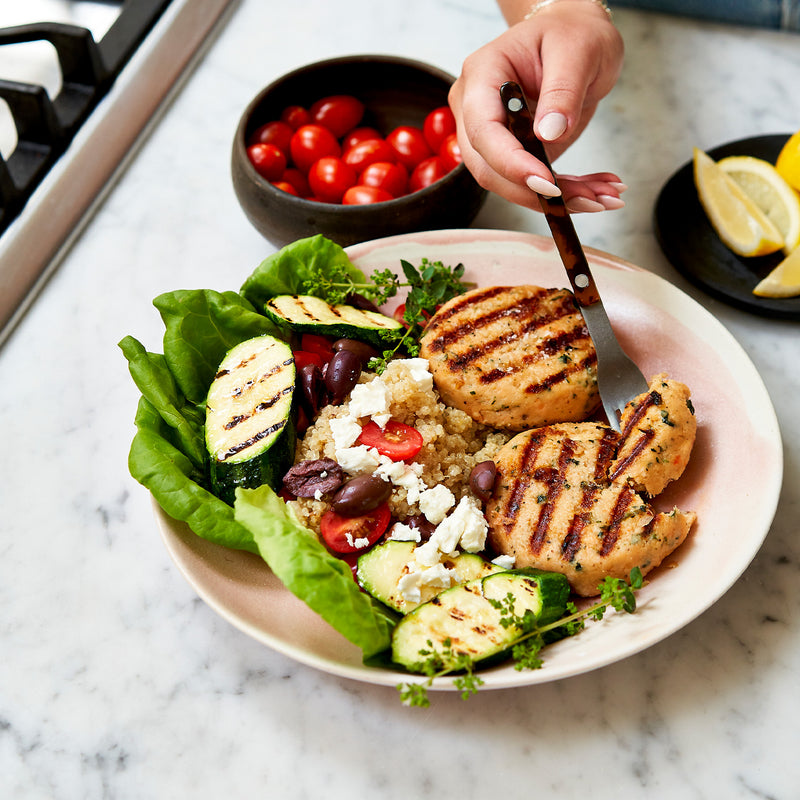 Plated salad with grilled salmon patties, zucchini, and cherry tomatoes on a marble surface.