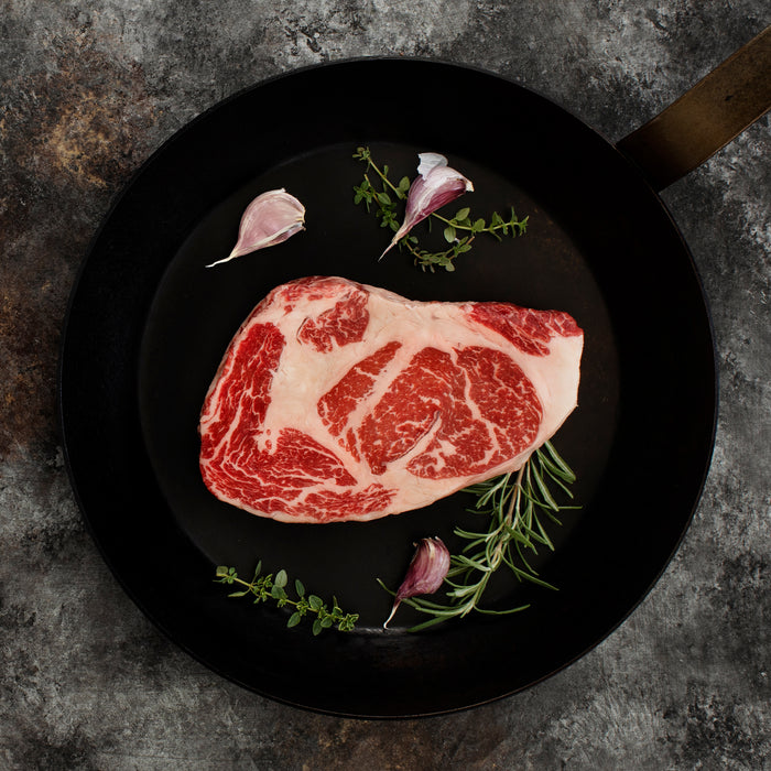 Raw Boneless Ribeye in a skillet with garlic and rosemary.
