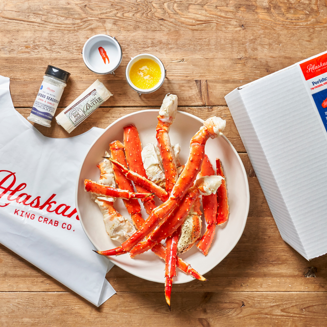 Alaskan King Crab Co. crab legs on a plate with seasonings and a box on a wooden table.