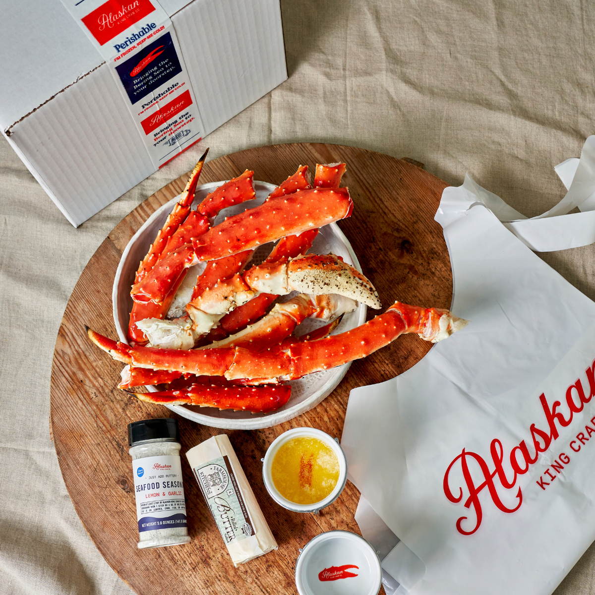 Alaskan King Crab legs on a wooden board with condiments and a branded bag.