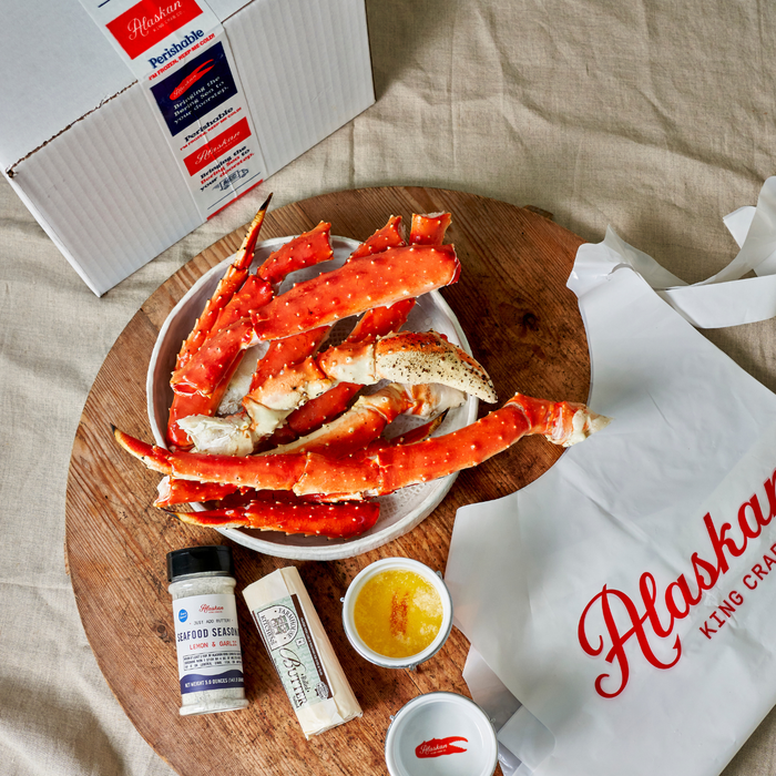 Alaskan King Crab legs on a wooden board with condiments and a branded bag.