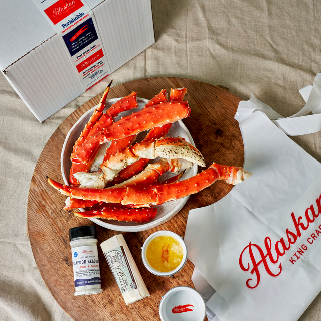 Alaskan King Crab legs on a wooden board with condiments and a branded bag.