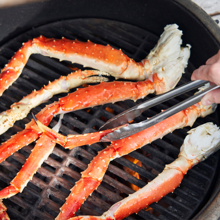 Grilling crab legs on a barbecue grill with tongs.