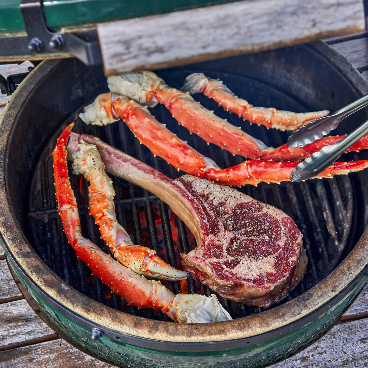 Steak and crab legs being cooked on a grill