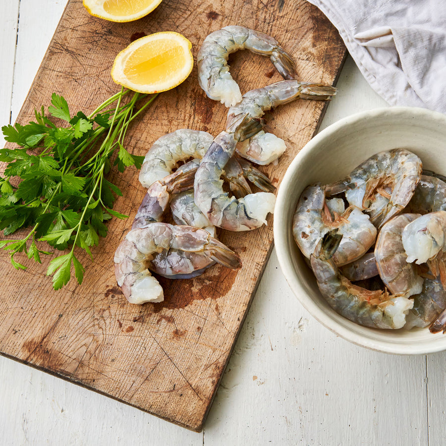 Raw U10 Oishii White Shrimp laying on a wooden cutting board and in a bowl.