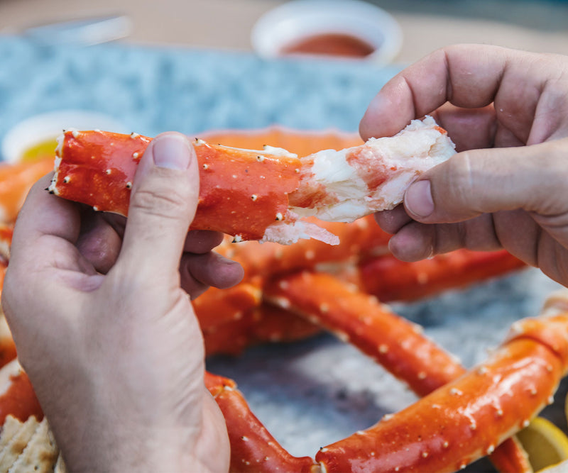 Hands pulling crab meat out of a king crab leg.